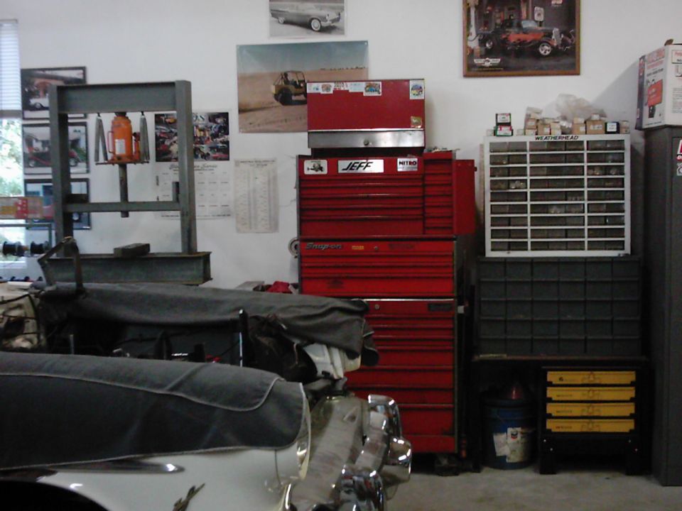 Garage interior with red tool chests, storage bins, and a covered vehicle in the foreground