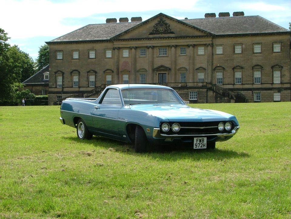 Blue 1970 Ford Ranchero with a white roof, parked on grass. Front grille and headlights are visible