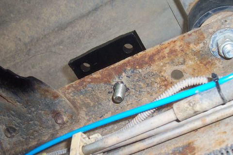 1994 Ford F-150 - A black bracket is attached to the rusty frame of a vehicle, with a blue cable secured by a zip tie.