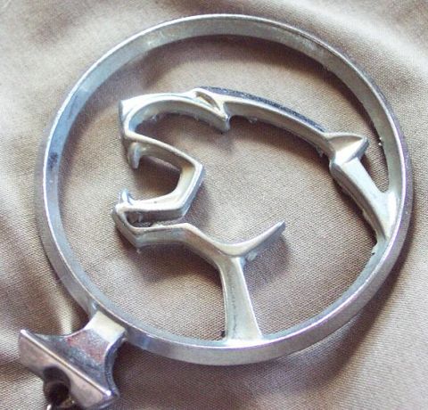 1985 Ford LTD Crown Victoria - A chrome cougar emblem, likely from a vehicle, is shown against a textured fabric background.