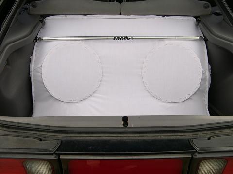 1997 Ford Probe - Straight-on view into an open hatch showing a subwoofer enclosure wrapped in white fabric with two round speaker cutouts stitched into the…