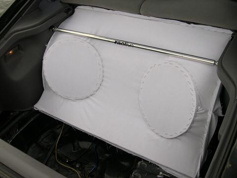 1997 Ford Probe - A bare MDF subwoofer box wrapped in white fabric sits test-fitted in a hatchback cargo area, with two circular speaker cutouts traced and s…