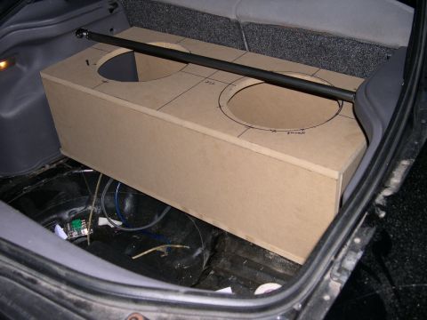1997 Ford Probe - Bare MDF subwoofer enclosure under construction, test-fit in a stripped hatch area with two cut speaker holes and pencil layout lines still…