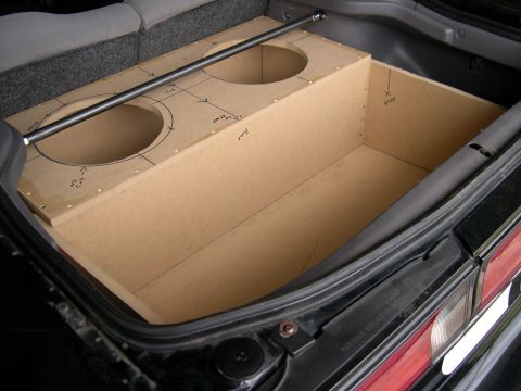 1997 Ford Probe - A raw MDF subwoofer enclosure under construction inside a car trunk, with two circular speaker cutouts, pencil layout lines and dimension n…