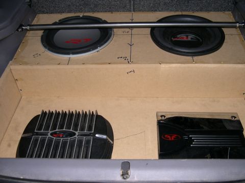 1997 Ford Probe - Bare MDF subwoofer enclosure and amp rack test-fitted in a hatchback cargo area, with two subwoofers mounted face-up in the top panel and p…