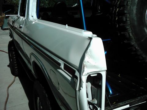 1978 Ford Bronco - The rear corner of a white SUV shows significant damage and missing parts, with a spare tire mounted inside.