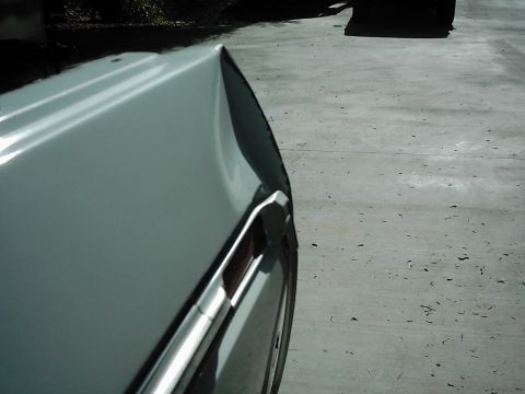 1978 Ford Bronco - The rear quarter panel of a white vehicle shows substantial damage and a chrome trim piece.