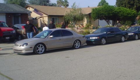 1993 Ford Taurus - A tan sedan, possibly a 2000 Ford Taurus, is parked on a residential street alongside other vehicles.