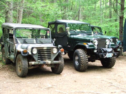 1996 Ford Bronco - A green Jeep and a camouflage Jeep are parked side-by-side on a dirt path in a forest.