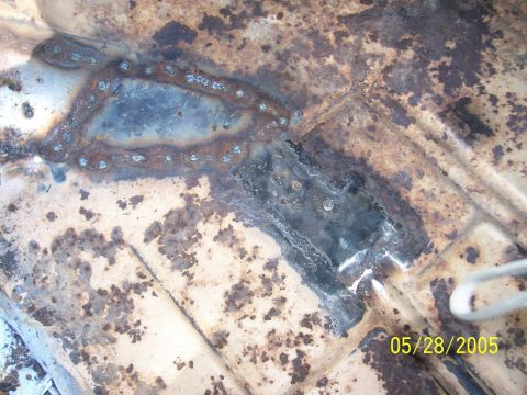 1979 Ford Bronco - Close-up of a heavily rusted vehicle floor showing repair welds and patches.