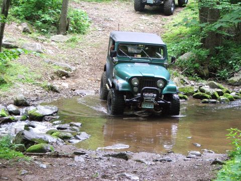 1996 Ford Bronco - A green Jeep navigates a rocky stream bed on an off-road trail, with another vehicle following behind.