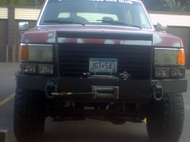 Red Ford Bronco front view with aftermarket bumper and winch. Paint is chipped, showing primer
