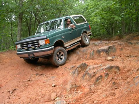 1990 Ford Bronco - Driver maneuvers a green 1990 Ford Bronco over a challenging rocky terrain during an off-road excursion.