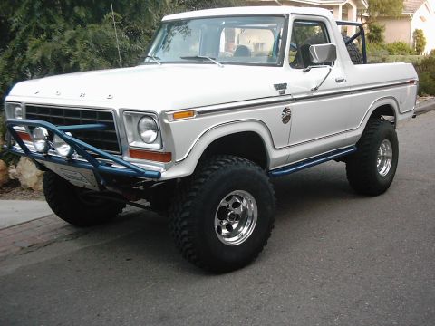 1978 Ford Bronco - White lifted full-size Ford Bronco with the rear hardtop removed, shot from the front three-quarter angle on a residential street. It has a…