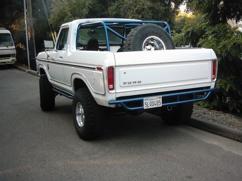 1978 Ford Bronco - Rear three-quarter view of a white lifted full-size Ford Bronco with the hardtop removed, showing the blue roll bar, a spare mud-terrain ti…