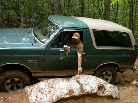 1990 Ford Bronco - This 1990 Ford Bronco is shown off-roading through a wooded area with rocky obstacles.