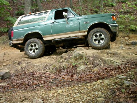 1990 Ford Bronco - Green 1990 Ford Bronco navigates a challenging off-road trail with muddy terrain.