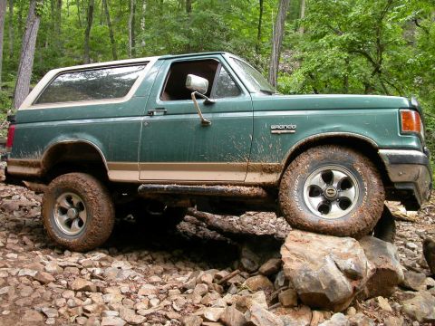 1990 Ford Bronco - A green 1990 Ford Bronco navigates a rocky trail in a wooded area.