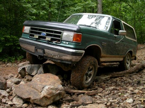 1990 Ford Bronco - A green Ford Bronco navigates a rocky trail in a wooded area.