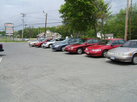 1998 Ford Taurus - A row of sedans, including a 1998 Ford Taurus, are parked in a lot on an overcast day.