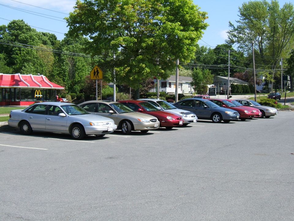 several sedans parked in a lot, including a silver Ford Taurus, with a McDonald's in the background
