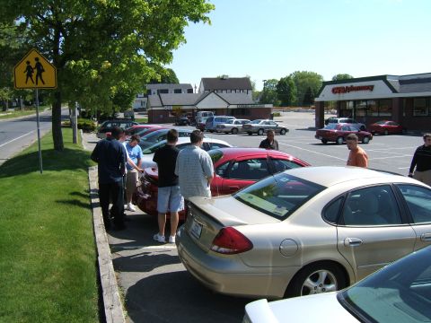 1998 Ford Taurus - A group of people stand around several cars in a parking lot, with a gold 1998 Ford Taurus prominently featured.