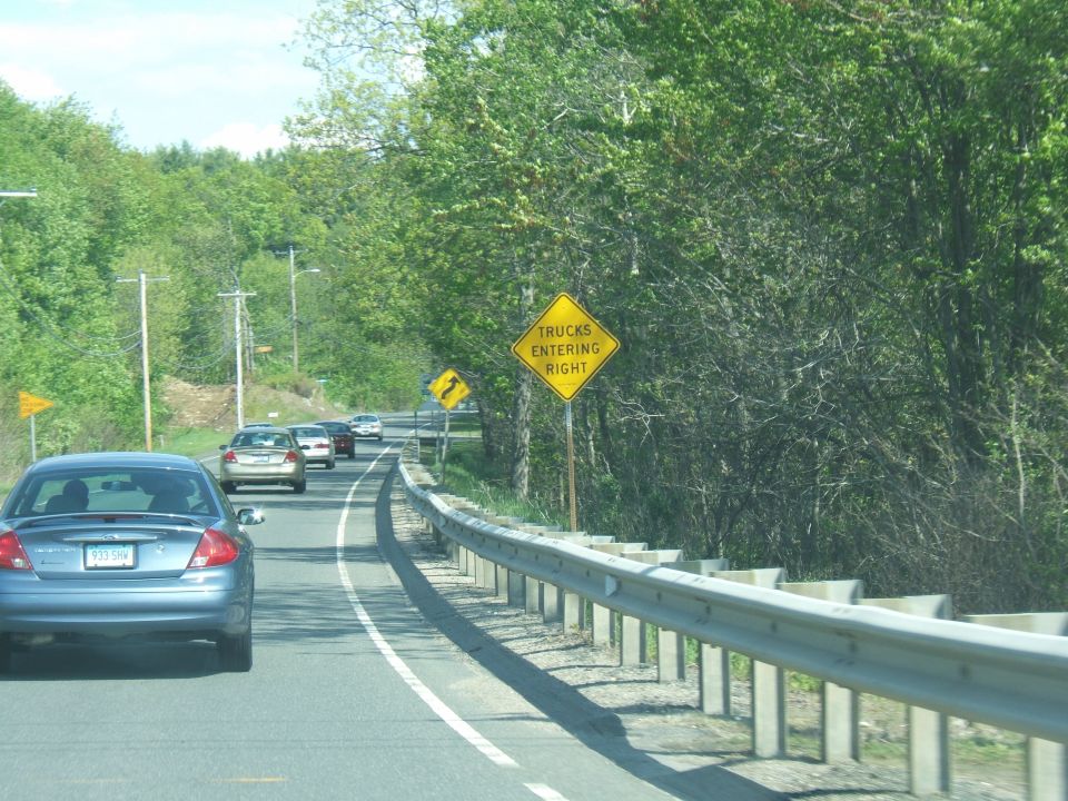 Cars driving on a highway with trees and a 'trucks entering right' sign