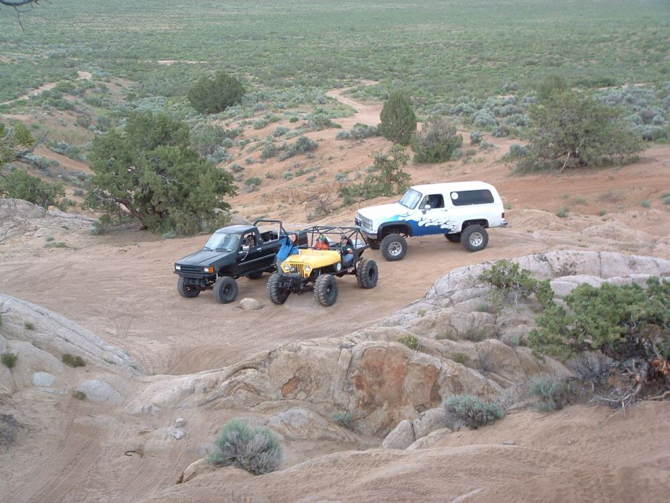 Three off-road rigs parked on slickrock in high-desert juniper terrain