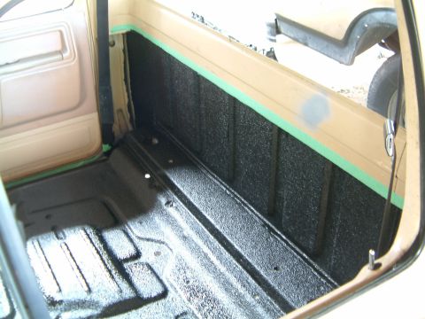 1985 Ford F-150 - The interior of a truck bed is shown after application of a black spray-on liner, with green masking tape along the upper edge.