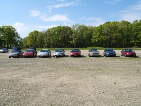 1998 Ford Taurus - Multiple sedans are parked in a lot on a sunny day.