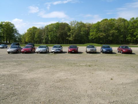 1998 Ford Taurus - A line of sedans are parked in an outdoor lot under a partly cloudy sky.