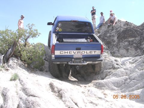 1994 Ford Bronco - A blue Chevrolet pickup truck navigates a rocky off-road trail with several people observing.