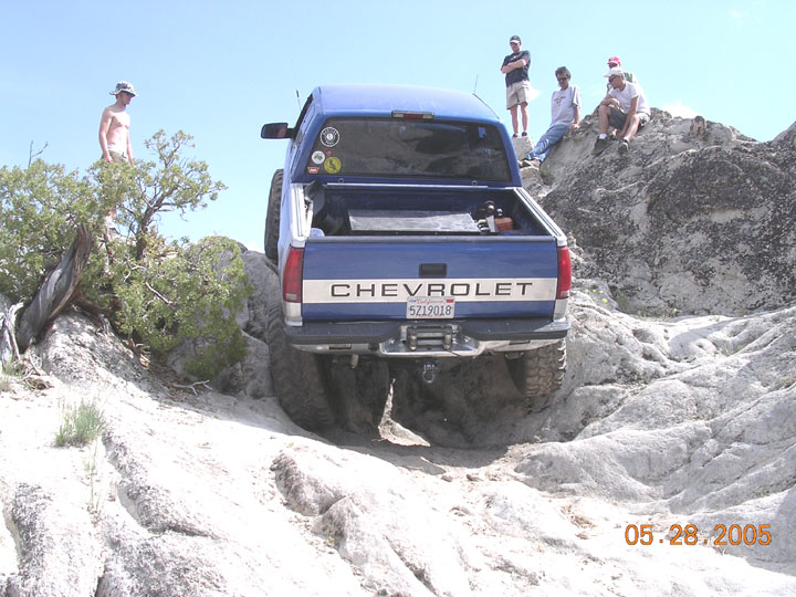 Blue Chevrolet pickup rock-crawling over granite, rear view with winch bumper