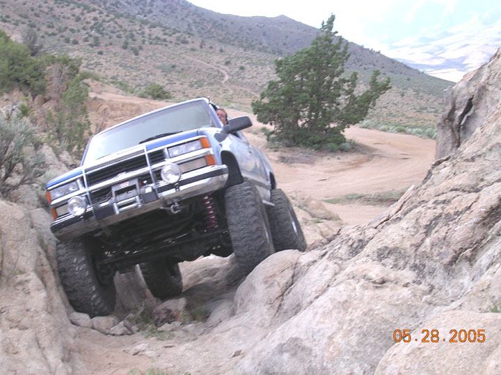 Lifted blue and silver Chevrolet 4x4 with brush guard climbing rocks on a desert trail