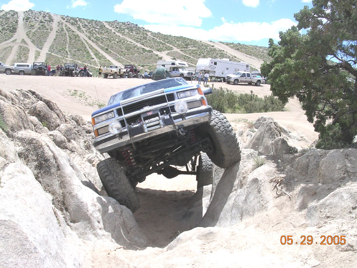 Lifted blue Chevrolet 4x4 with winch climbing out of a rock bowl at an off-road event