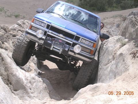 1994 Ford Bronco - A blue truck navigates a rocky trail with its front tire lifted.