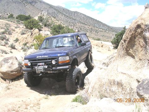 1994 Ford Bronco - A blue SUV navigates a rocky off-road trail with a person driving.
