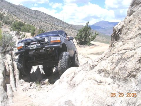1994 Ford Bronco - Off-road Bronco tackles a challenging rocky terrain under a partly cloudy sky.