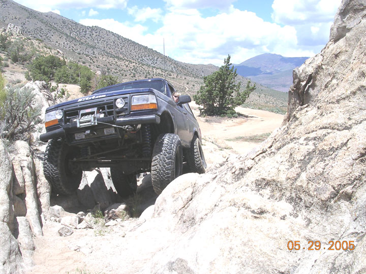 Dark blue lifted Ford Bronco climbing rocks on a mountain off-road trail with front winch.