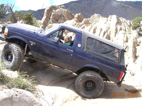 1994 Ford Bronco - A blue 1994 Ford Bronco is shown off-roading over large rocks.