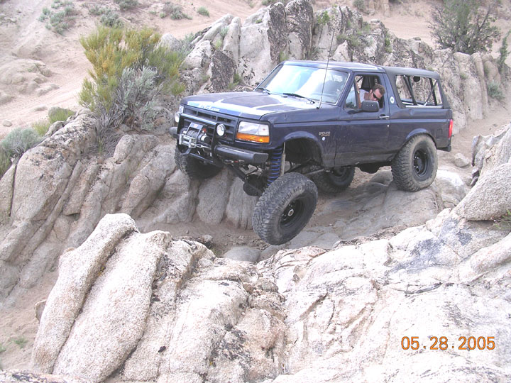 Dark blue lifted Ford Bronco with winch crawling over desert rocks