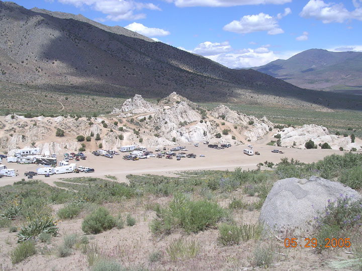 Distant desert campsite with many parked RVs and vehicles below mountains