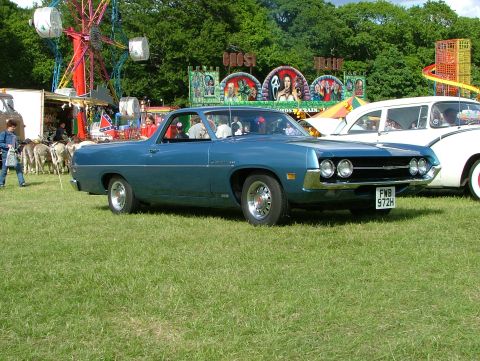 1970 Ford Ranchero - A blue 1970 Ford Ranchero is parked on a grassy field with a Ferris wheel and carnival attractions in the background.