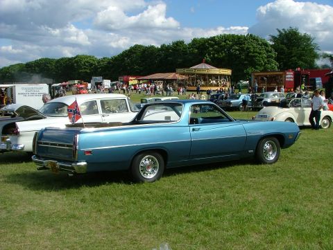 1970 Ford Ranchero - A blue 1970 Ford Ranchero is parked on a grassy field at an outdoor event, with a carousel and other vehicles visible.
