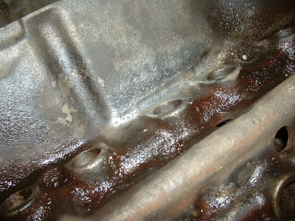 Close-up of a cast-iron V8 engine block lifter valley coated in brown oil varnish