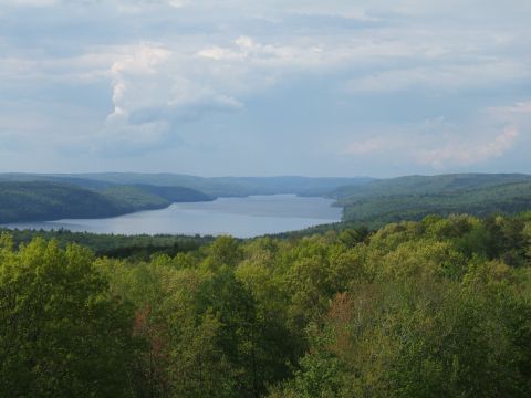 1998 Ford Taurus - A wide view of a lake surrounded by lush green forests and rolling hills under a dramatic sky.