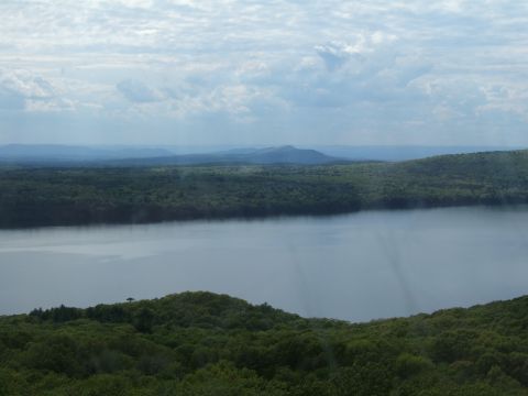 1998 Ford Taurus - A wide view of a lake with misty shores, bordered by dense forests and distant hills under a cloudy sky.