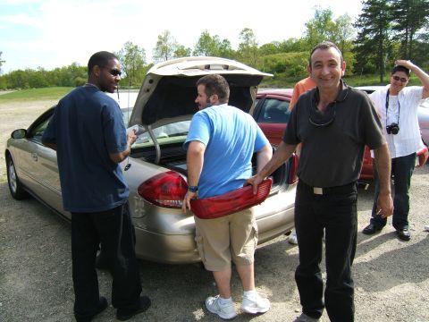 1998 Ford Taurus - Three men stand around a car with its trunk open, one man holds a detached taillight.