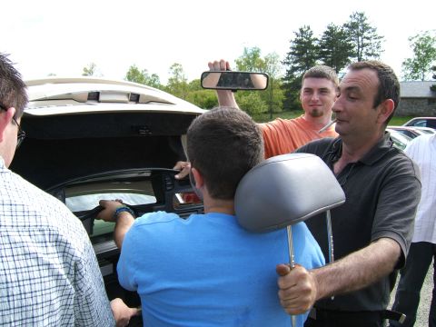 1998 Ford Taurus - Several men are seen around the open trunk of a car, with one man holding a car headrest.
