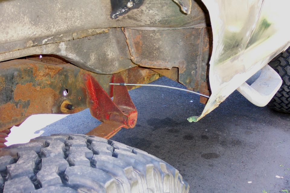 Underside view of rusty truck frame and red bracket with damaged body panel